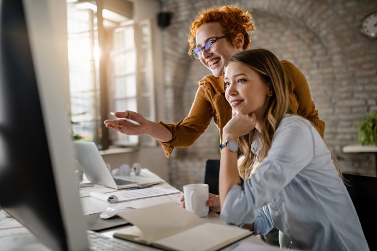 happy female entrepreneurs reading email computer while working together office focus is redhead woman